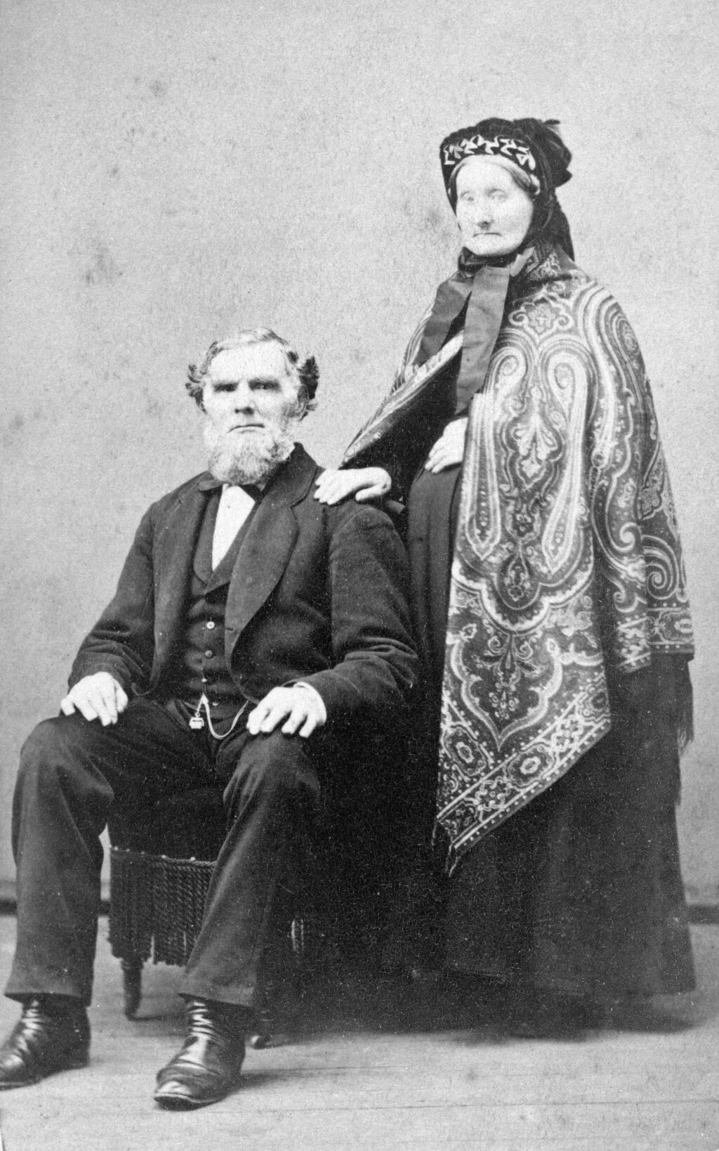 An old black and white photograph of a seated man in a suit and a standing woman with a patterned shawl.